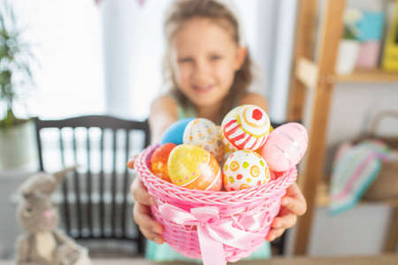 A preschool girl paints eggs for the bright holiday of Easter. Happy at the table with paints and eggsの写真素材