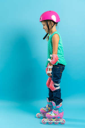 Little girl child in protective clothing helmet knee pads elbow pads with rollers on a blue backgroundの写真素材