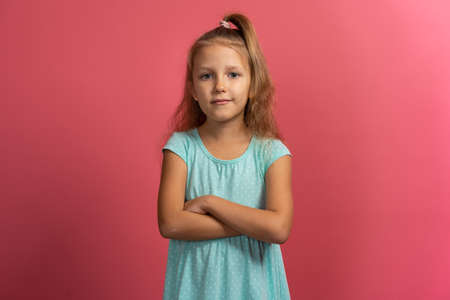 Little beautiful child girl in blue dress with crossed arms on pink backgroundの写真素材