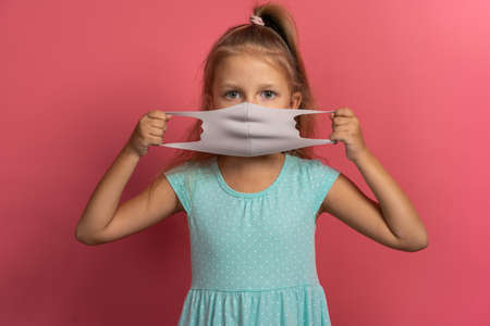 Little beautiful child girl in blue dress with face mask on pink backgroundの写真素材