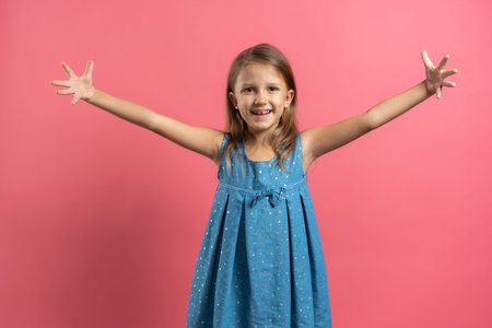 Little beautiful child girl in blue dress spread her arms wide wants to hug on pink backgroundの写真素材