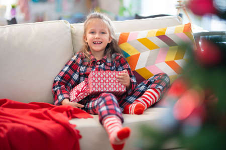 Little Girl In Pajamas Decorates Christmas Tree With Toys And Gift At Home In Roomの写真素材