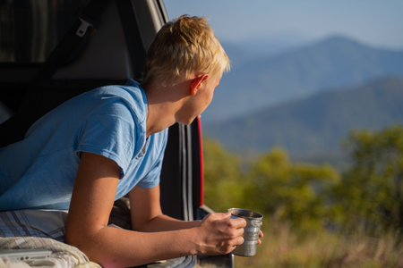 A young man is resting in nature with an off-road vehicle Drinks coffee from an iron mug. Resting in...