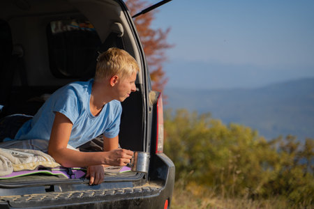 A young man is resting in nature with an off-road vehicle Drinks coffee from an iron mug. Resting in...