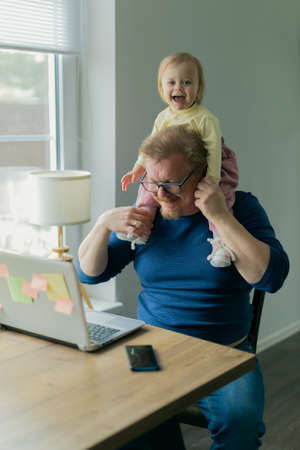 A freelance man father tries to work at home on a computer on the Internet and sits with a small child who prevents him from doing businessの写真素材
