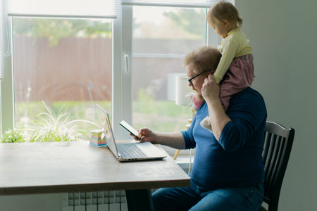 A freelance man father tries to work at home on a computer on the Internet and sits with a small...