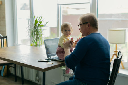 A freelance man father tries to work at home on a computer on the Internet and sits with a small...