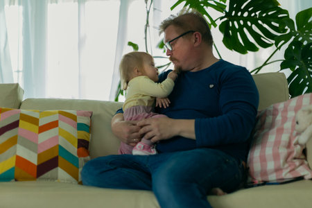 Father man sitting at home with a small child on the sofa on the against the window