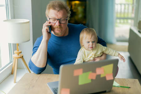 A freelance man father tries to work at home on a computer on the Internet and sits with a small child who prevents him from doing businessの写真素材