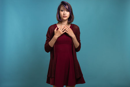 Beautiful brunette girl with dyed purple hair shows emotions on a blue background