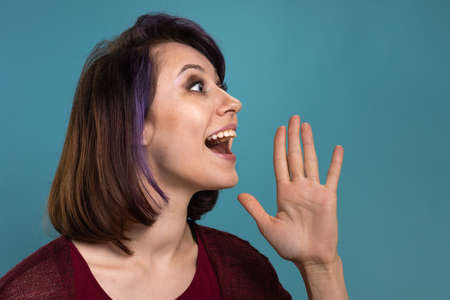 Beautiful brunette girl with dyed purple hair shows emotions on a blue backgroundの写真素材