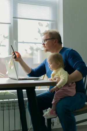 A freelance man father tries to work at home on a computer on the Internet and sits with a small...