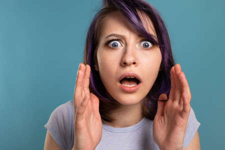 A beautiful young brunette girl in a T-shirt and breeches on a blue background shows different emotions smiles, is surprised and has funの写真素材