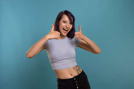 A beautiful young brunette girl in a T-shirt and breeches on a blue background shows different emotions smiles, is surprised and has funの写真素材