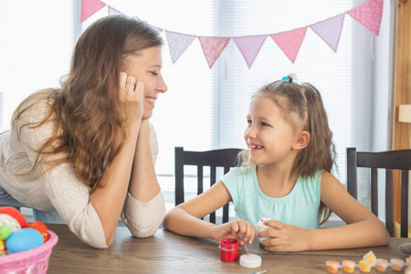 Mom and daughter are painting eggs for the bright holiday of Easter. Sit for happy with paints