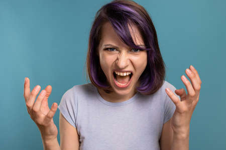 A beautiful young brunette girl in a T-shirt and breeches on a blue background shows different emotions smiles, is surprised and has funの写真素材