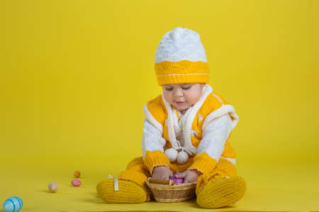 Little child one year age girl in yellow clothes sits with easter eggs on a yellow background expresses emotionsの写真素材