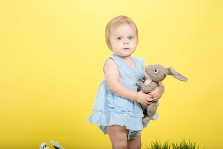 Little baby girl on green grass and yellow background in the ears of an easter bunny with painted...