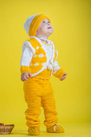 Little child one year age girl in yellow clothes look up on a yellow background expresses emotionsの写真素材