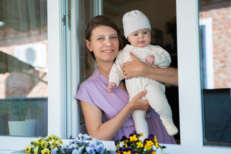 Mother woman with a newborn baby looking out the window from her home while being isolated from...