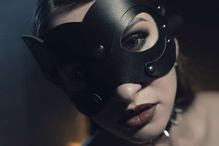 Beautiful woman in black lingerie and leather belt dominates in cat mask the background of lamps and smokeの写真素材