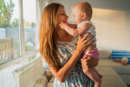 Portrait of a woman mother with a newborn baby in her arms at home next to a window in the roomの写真素材