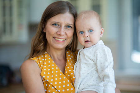 Beautiful young brunette woman in dress with baby in the kitchen at homeの写真素材