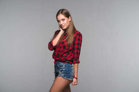 Young beautiful woman teenager in a red checked shirt and torn denim shorts on a gray backgroundの写真素材