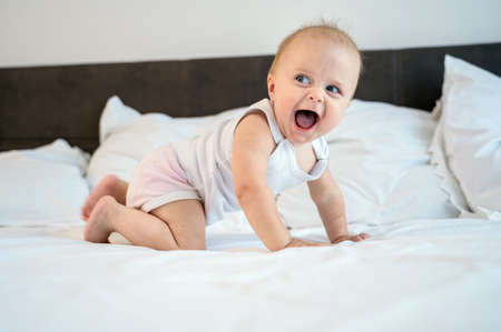 Little baby child lies and rejoices on the bed in the bedroom at homeの写真素材
