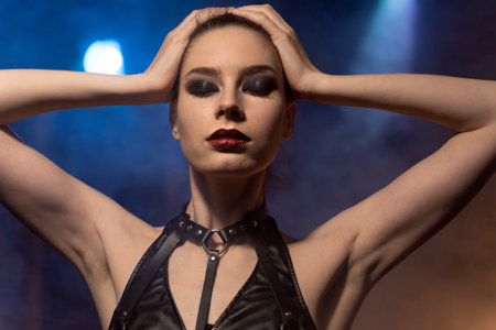Beautiful woman in black lingerie and leather belt dominates the background of lamps and smoke