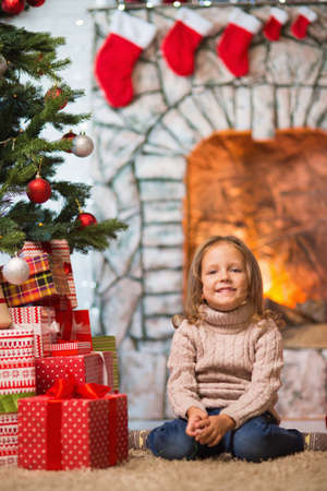 Little girl child at home at the fireplace celebrates Merry Christmas with giftsの写真素材