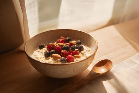 A bowl of creamy oatmeal is topped with vibrant raspberries, blueberries, and crunchy walnuts. Soft sunlight illuminates the scene on a bright morning.の素材