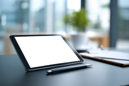 A blank tablet is positioned on a wooden table beside a small green plant in a contemporary cafe. Soft natural light fills the space, creating a vibrant atmosphere.の素材