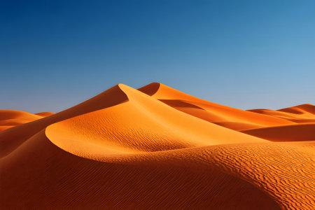 Warm golden sand dunes rise and fall gracefully under a clear blue sky. This serene desert landscape captures the beauty of nature in a peaceful setting.の素材
