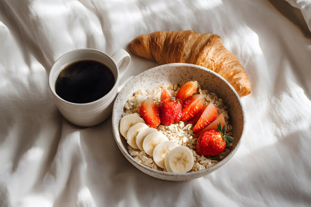 A cozy breakfast scene with a bowl of oatmeal topped with fresh strawberries, blueberries, bananas, and blackberries. A croissant and a cup of coffee complete the meal.の素材