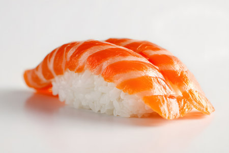 Two beautifully arranged pieces of sushi sit on a white plate, showcasing vibrant orange salmon slices topped with sesame seeds, highlighting skillful culinary presentation.の素材
