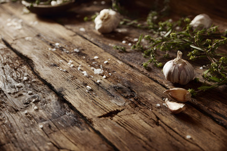 Garlic cloves and crystals of coarse salt are arranged on a weathered wooden surface, showcasing ingredients for flavoring dishes. The rustic setting highlights culinary preparation.の素材