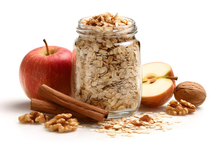 Jars filled with rolled oats sit beside fresh apples and walnuts on a white surface, infused with the warm scent of cinnamon. Perfect for a healthy autumn breakfast.の素材