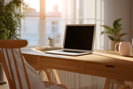 A well-lit workspace features a laptop on a wooden table. Sunlight streams through the window, casting shadows. Plants add life to the setting, enhancing the cozy feel.の素材