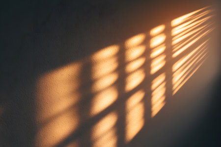 Natural light streams through a window, casting soft, striped shadows on a wooden floor in a simple, uncluttered room during golden hour. The warm tones create a serene atmosphere.の素材