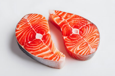 Four fresh salmon fillets are neatly arranged on a white background, showing their vibrant pink color and unique texture, ideal for various culinary uses.の素材