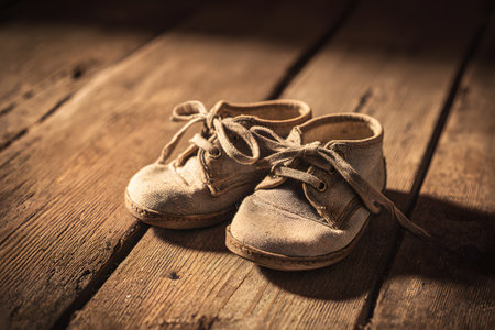 An old pair of brown leather shoes sits on a weathered wooden bench, illuminated by soft light that highlights their worn texture and laces.の素材