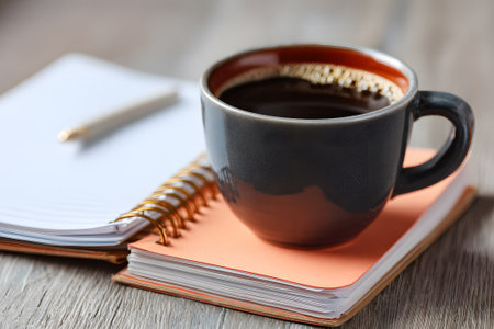 A warm cup of coffee sits beside a notebook and pen on a rustic wooden table, creating a tranquil workspace. Perfect for early morning writing or brainstorming.の素材