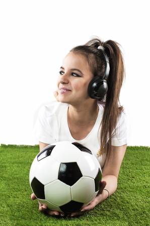 Portrait of a handsome female a holding a football and listening music on headphones isolated on white backgroundの写真素材