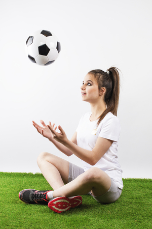 Teen girl juggling soccer ball with her hands. Gray background.の写真素材