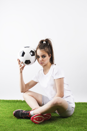 Beautiful girl in a sports T-shirt with a ball on a gray background.Sad beautiful teenager  crying over her national football team's loss in soccer championship.Gray backgroundの写真素材