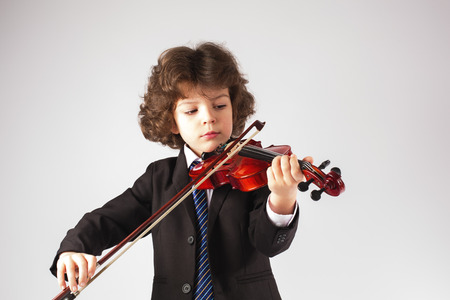 Little curly boy playing a musical instrument. Gray background.の写真素材