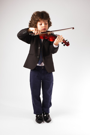 Clever little violinist in a business suit playing a musical instrument. Gray background.の写真素材