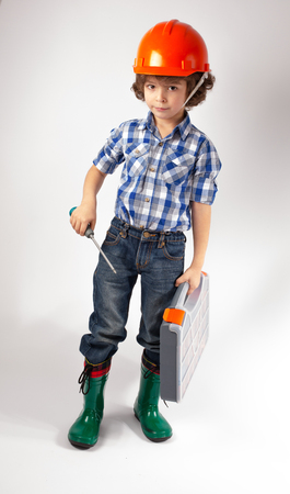 Little curly-haired worker in a helmet is a tool in the hands. Gray background.の写真素材