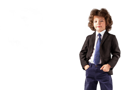 Curly stylish boy standing and looking at the camera in a business suit. Hands holding in their pockets. White background.の写真素材